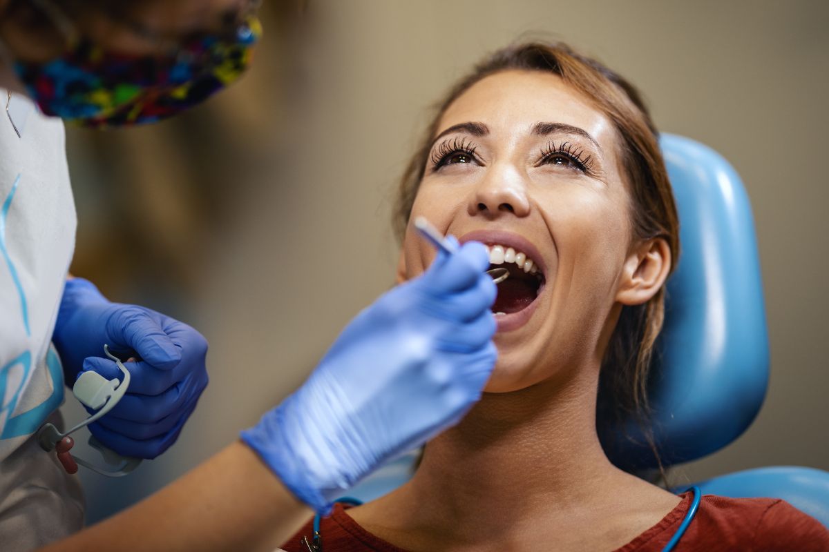 cosmetic dental checkup Cosmetic dentist examining a smiling patient’s teeth during a dental consultation.