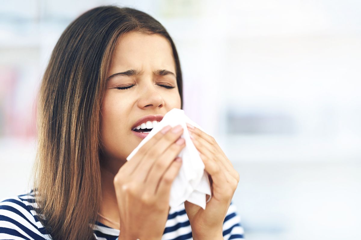 seasonal allergies A woman sneezing into a tissue due to seasonal allergies, illustrating sinus pressure that can affect oral health.