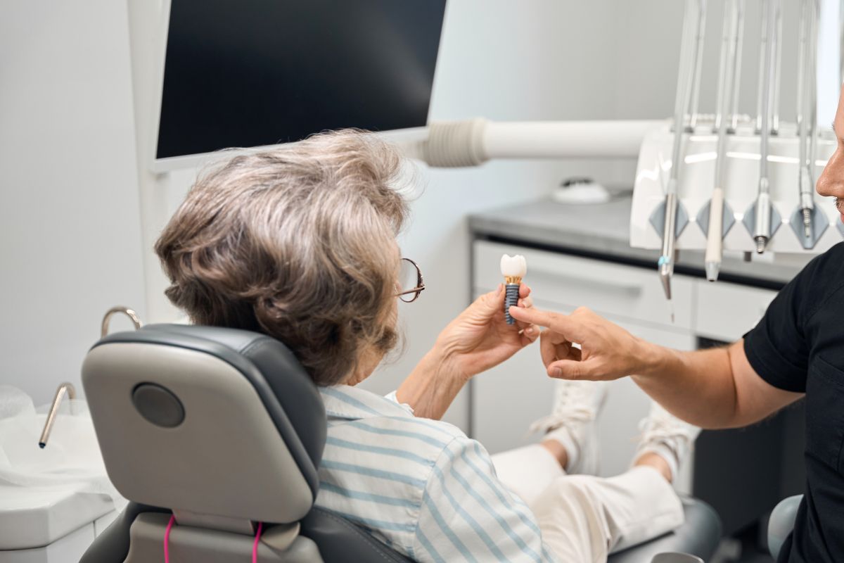 Patient discussing dental implant treatment with a dentist while reviewing a tooth implant model.