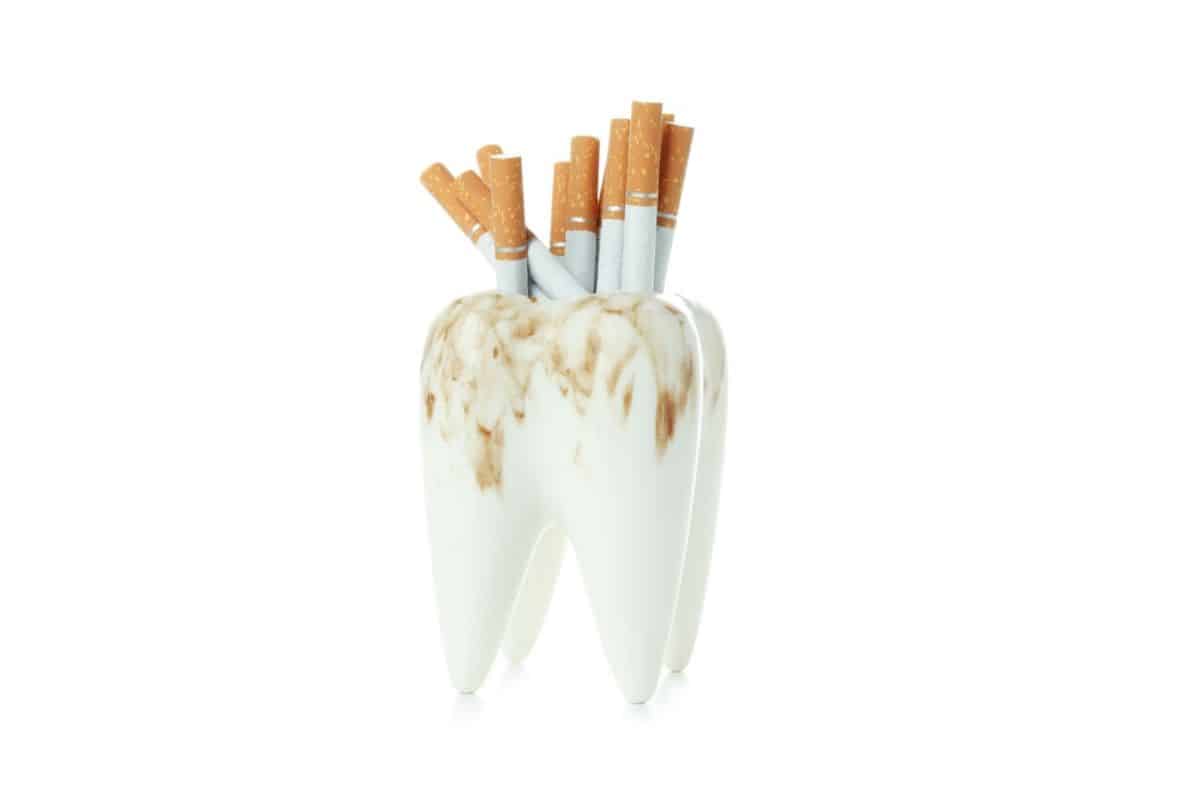 Cigarettes placed inside a stained tooth model representing tobacco-related tooth discoloration.